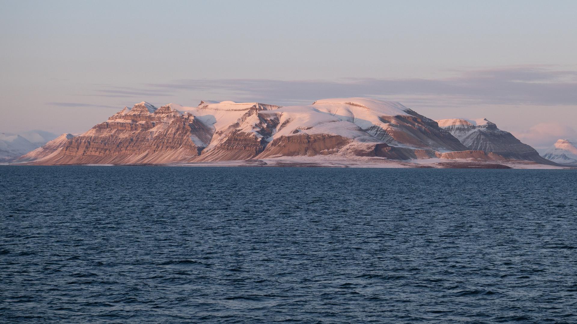Eine mit Schnee bedeckte Gebirgskette im Isfjord im Licht der untergehenden Sonne.