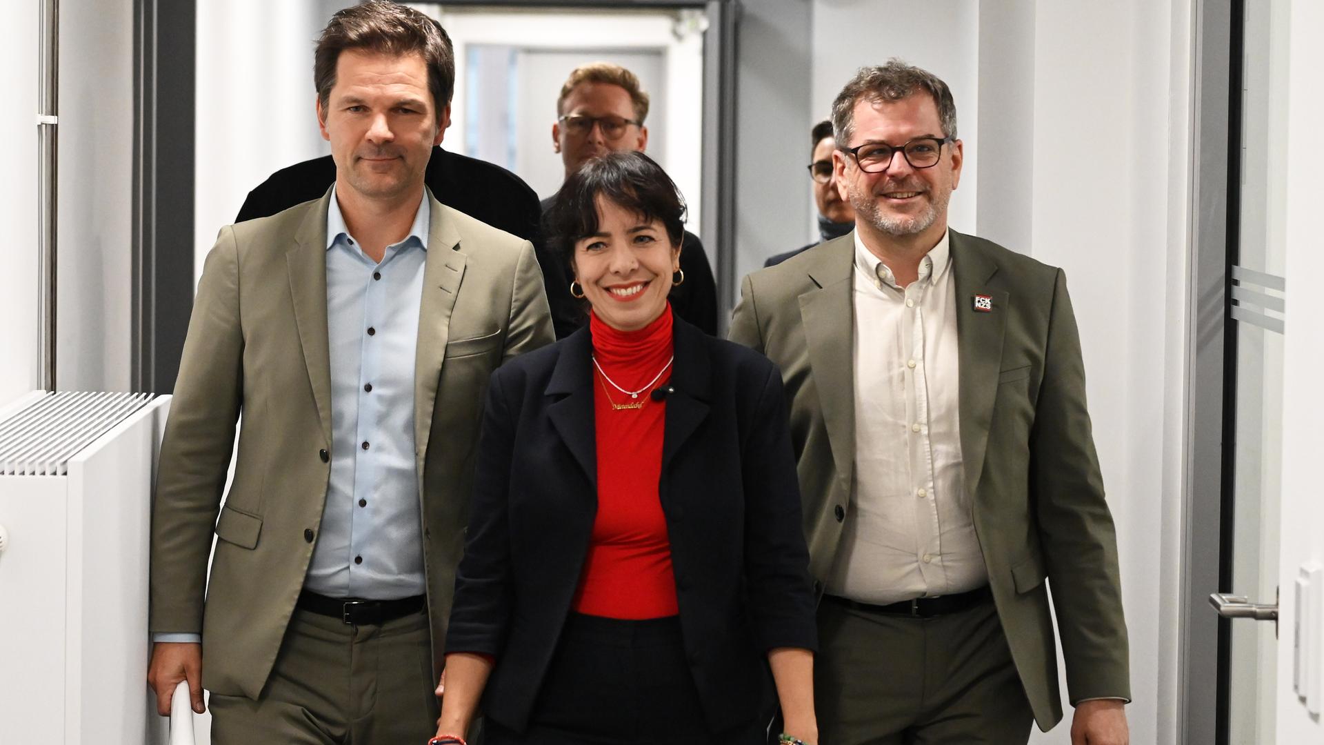 Werner Graf (Bündnis 90/Die Grünen), Elif Eralp (Die Linke) und Steffen Krach (SPD) (v.r.n.l) laufen nebeneinander durch einen Flur und lächeln dabei Werner Graf (Bündnis 90/Die Grünen), Elif Eralp (Die Linke) und Steffen Krach (SPD) (v.r.n.l) laufen nebeneinander durch einen Flur und lächeln dabei