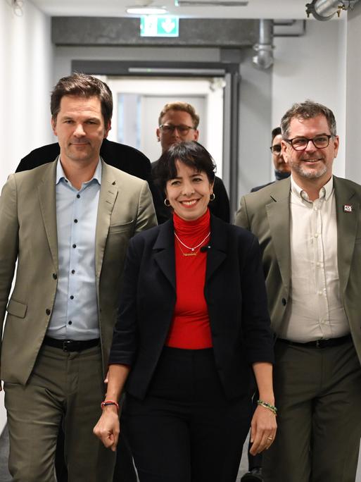 Werner Graf (Bündnis 90/Die Grünen), Elif Eralp (Die Linke) und Steffen Krach (SPD) (v.r.n.l) laufen nebeneinander durch einen Flur und lächeln dabei Werner Graf (Bündnis 90/Die Grünen), Elif Eralp (Die Linke) und Steffen Krach (SPD) (v.r.n.l) laufen nebeneinander durch einen Flur und lächeln dabei