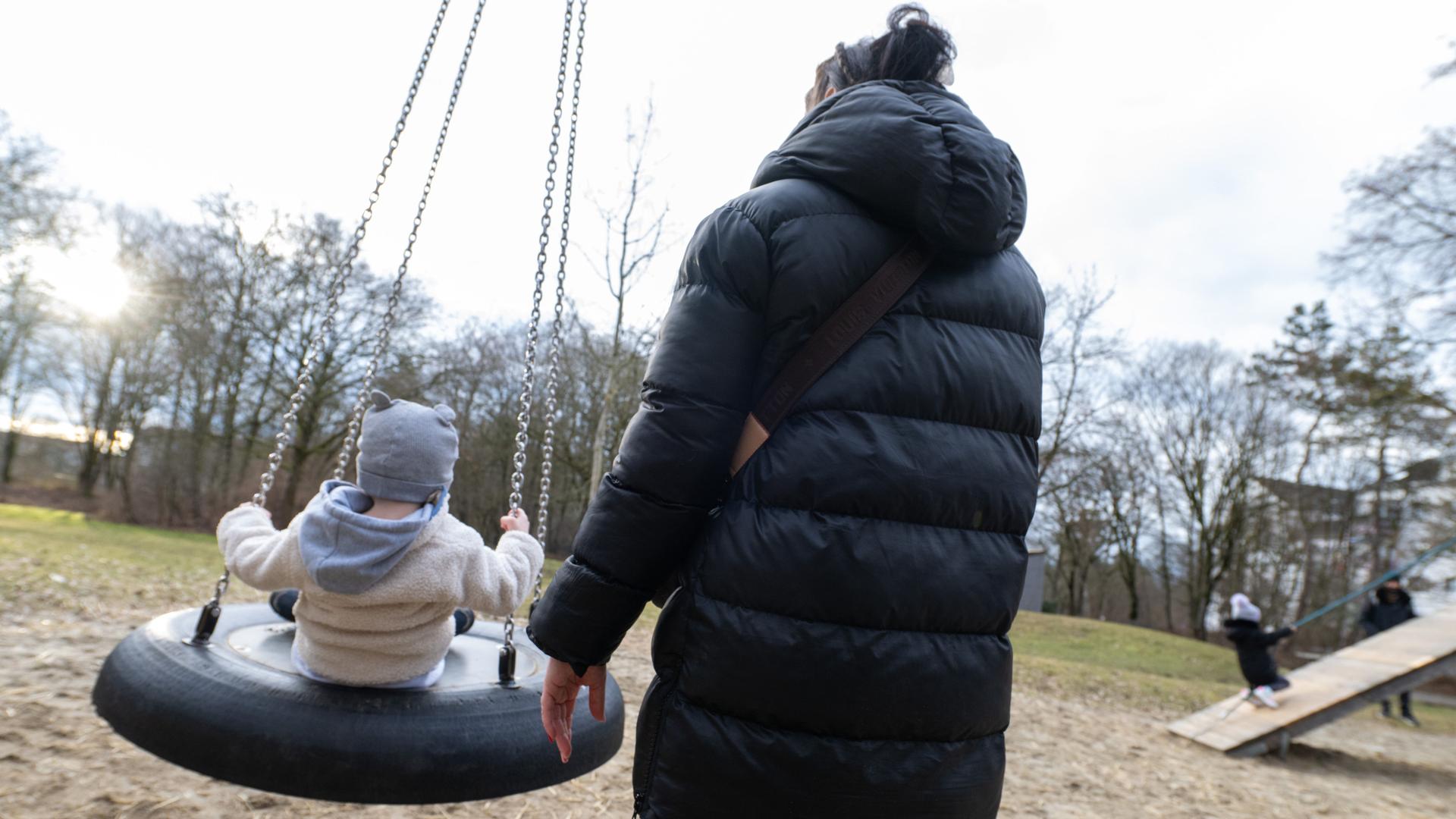 Das Bild zeigt eine Mutter mit ihrem Kleinkind auf einem Spielplatz. Beide sind von hinten fotografiert, so dass ihre Gesichter nicht zu erkennen sind. Das Bild zeigt eine Mutter mit ihrem Kleinkind auf einem Spielplatz. Beide sind von hinten fotografiert, so dass ihre Gesichter nicht zu erkennen sind.