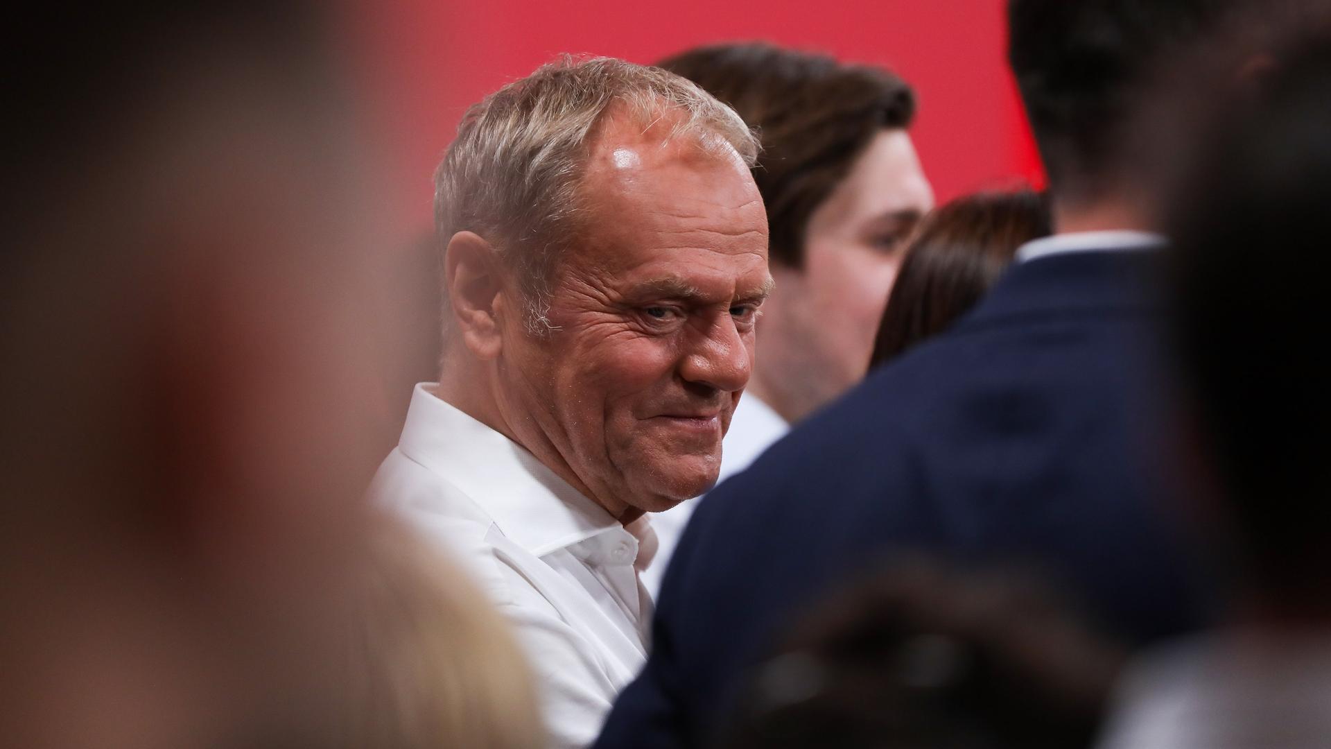 Polens Premierminister Donald Tusk steht auf einer Wahlveranstaltung zwischen mehreren Menschen und blickt zur Seite.