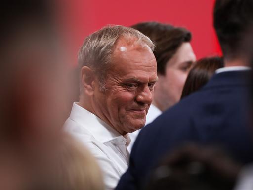 Polens Premierminister Donald Tusk steht auf einer Wahlveranstaltung zwischen mehreren Menschen und blickt zur Seite.