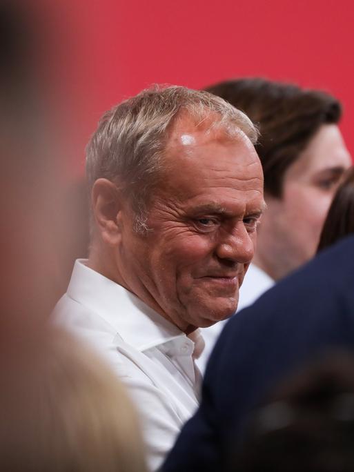 Polens Premierminister Donald Tusk steht auf einer Wahlveranstaltung zwischen mehreren Menschen und blickt zur Seite.