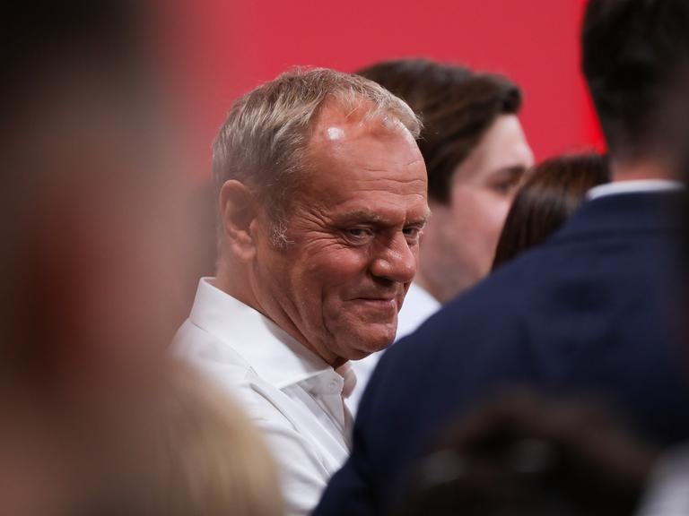 Polens Premierminister Donald Tusk steht auf einer Wahlveranstaltung zwischen mehreren Menschen und blickt zur Seite.