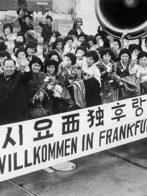 "Herzlich Willkommen in Frankfurt Deutschland" steht auf einem Spruchband, mit dem eine große Gruppe Krankenschwestern aus Südkorea im Jahr 1966 auf dem Rhein-Main-Flughafen begrüßt wird.