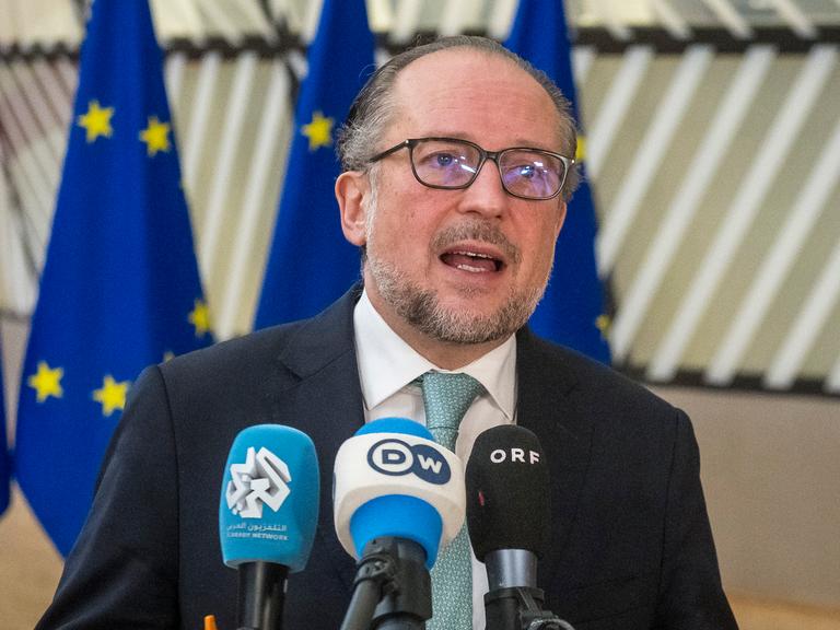 Der Österreichische Aussenminister Alexander Schallenberg steht vor drei EU-Flaggen und spricht in Mikrofone von Pressevertretern.