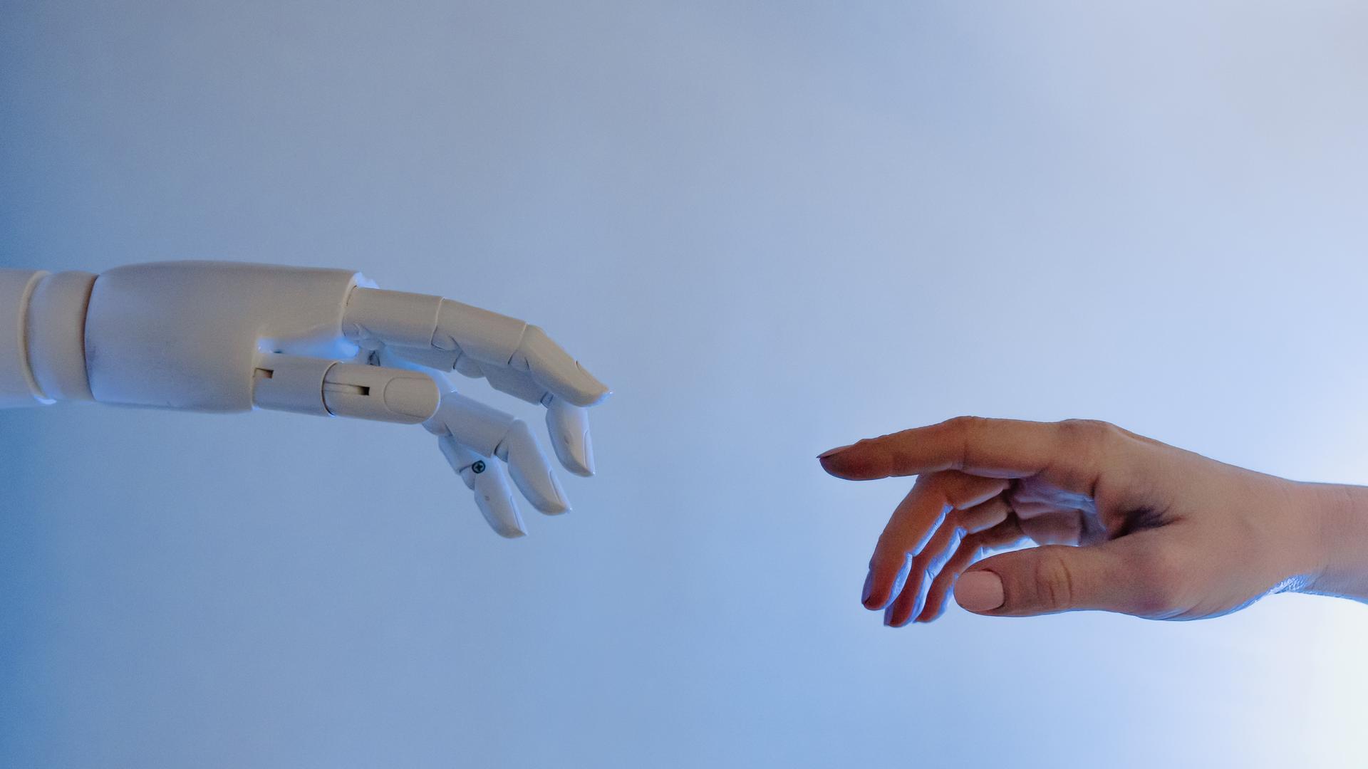Symbolbild Künstliche Intelligenz. Eine Roboterhand trifft auf eine menschliche Hand.