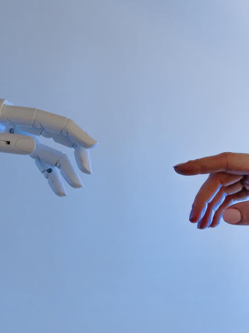 Symbolbild Künstliche Intelligenz. Eine Roboterhand trifft auf eine menschliche Hand.