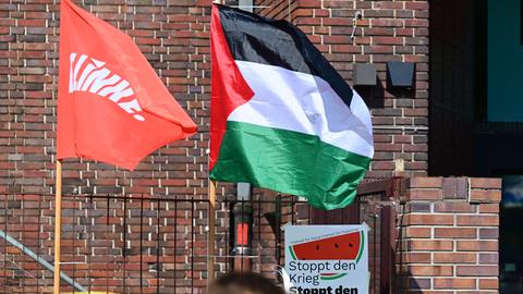 Fahne der Partei "Die Linke" und palästinensische Flagge bei einer Veranstaltung in Berlin-Neukölln. Auf einem Plakat steht "Stoppt den Krieg. Stoppt den Völkermord".