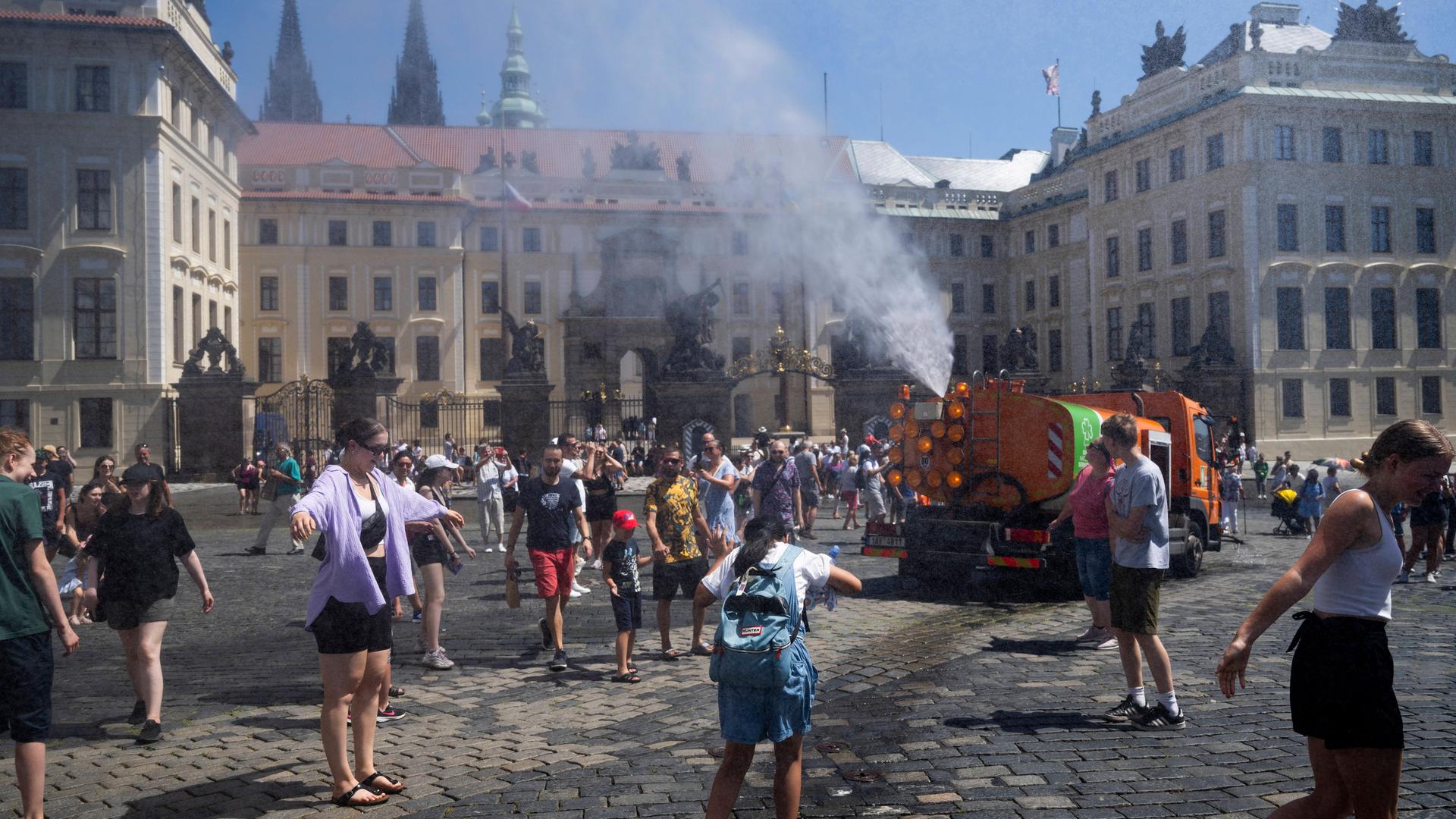 Wegen der hohen Temperaturen sprüht ein Wagen in der tschechischen Hauptstadt Prag Wasser zur Abkühlung auf die Straßen. Menschen laufen durch den Wasserstrahl und erfrischen sich.