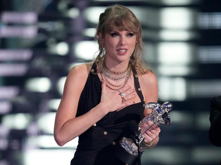 Die Musikerin Taylor Swift steht auf der Bühne, hält einen MTV Award in der Hand und macht eine Geste der Rührung.
