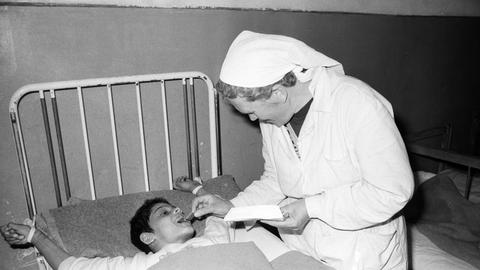 Eine Pflegerin füttert auf dem Schwarzweißbild von 1990 einen an ein Bettgestell gefesselten Jungen in einem Heim in Badacin, Rumänien.