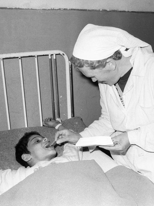 Eine Pflegerin füttert auf dem Schwarzweißbild von 1990 einen an ein Bettgestell gefesselten Jungen in einem Heim in Badacin, Rumänien. Eine Pflegerin füttert auf dem Schwarzweißbild von 1990 einen an ein Bettgestell gefesselten Jungen in einem Heim in Badacin, Rumänien.