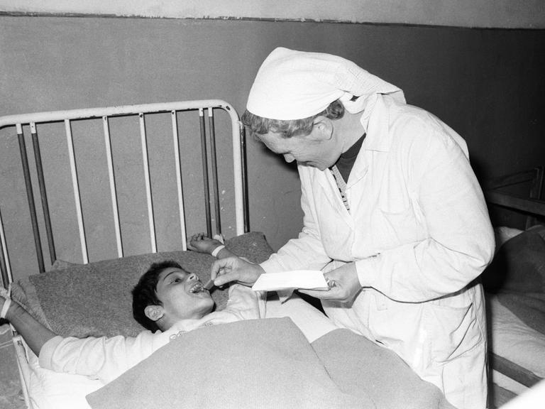 Eine Pflegerin füttert auf dem Schwarzweißbild von 1990 einen an ein Bettgestell gefesselten Jungen in einem Heim in Badacin, Rumänien. Eine Pflegerin füttert auf dem Schwarzweißbild von 1990 einen an ein Bettgestell gefesselten Jungen in einem Heim in Badacin, Rumänien.