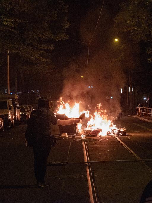 Am Vorabend des "Tag X" anlässlich des Antifa Ost Prozesses zogen mehrere Hundert Menschen aus der linksautonomen und linksextremen Szene durch den Leipziger Stadtteil Connewitz. Mülleimer brennen auf der Mitte einer Straße. 