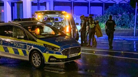 Das Bild ist etwas unscharf. Es ist dunkel. Zwei Polizeiautos stehen auf einer Straße. Polizisten bringen den kaum erkennbaren Täter zu einem der Fahrzeuge. 