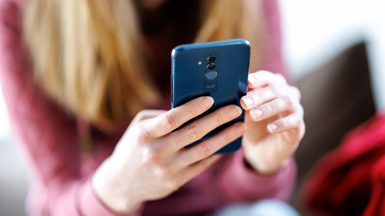 Eine junge Frau sitzt und hält ein Smartphone mit beiden Händen. Sie blickt auf das Display. Ihr Gesicht ist unscharf im Hintergrund.