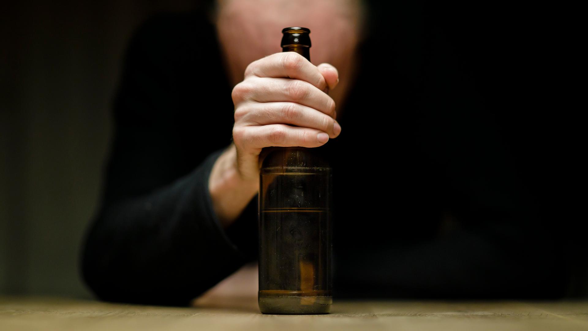 Ein Mann sitzt an einem Tisch und hält eine Flasche Bier in der Hand.