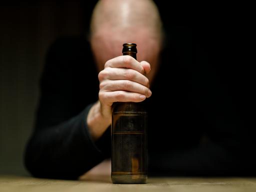 Ein Mann sitzt an einem Tisch und hält eine Flasche Bier in der Hand.