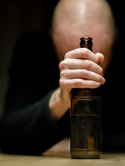 Ein Mann sitzt an einem Tisch und hält eine Flasche Bier in der Hand.