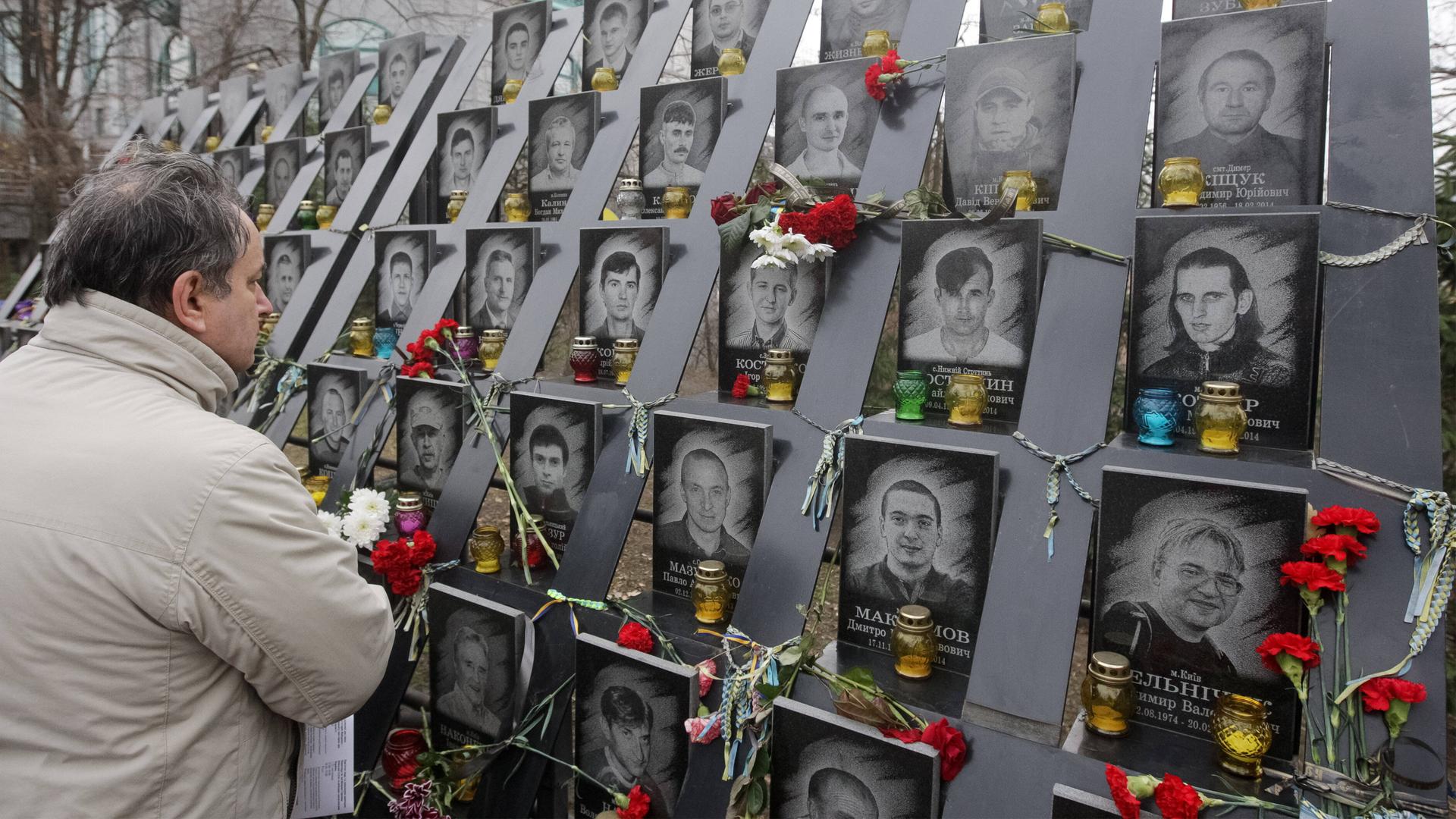 Ein Mann steht vor einer mit roten Rosen verzierten Gedenktafel mit Fotos und Namen der über 100 Menschen, die bei der Niederschlagung der Euromaidan-Proteste 2014 in Kiew ums Leben gekommen sind.