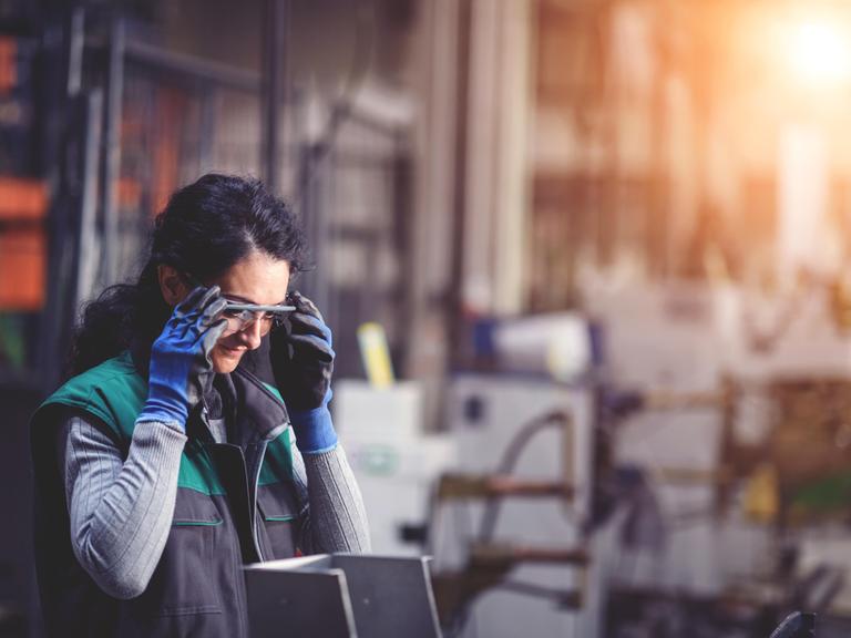 Eine Arbeiterin trägt eine Sicherheitsbrille und steuert Drehmaschinen zum Bohren von Komponenten in einer Fabrik zur Herstellung von Metalldrehmaschinen.