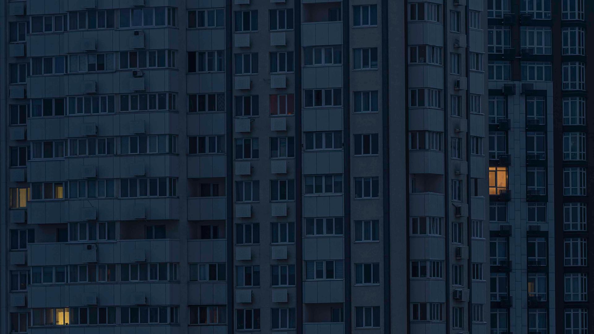 Ein Hochhaus in der Dunkelheit, nur aus wenigen Fenstern kommt Licht.