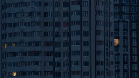 Ein Hochhaus in der Dunkelheit, nur aus wenigen Fenstern kommt Licht.