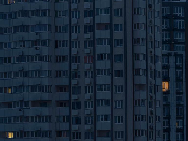 Ein Hochhaus in der Dunkelheit, nur aus wenigen Fenstern kommt Licht.