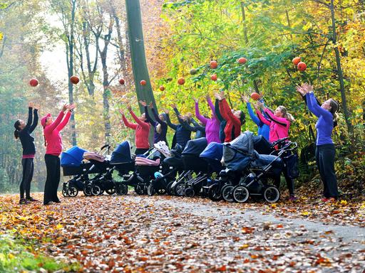 Zu sehen sind Mütter mit Kinderwagen, die im Wald stehen und Bälle in die Luft werfen.