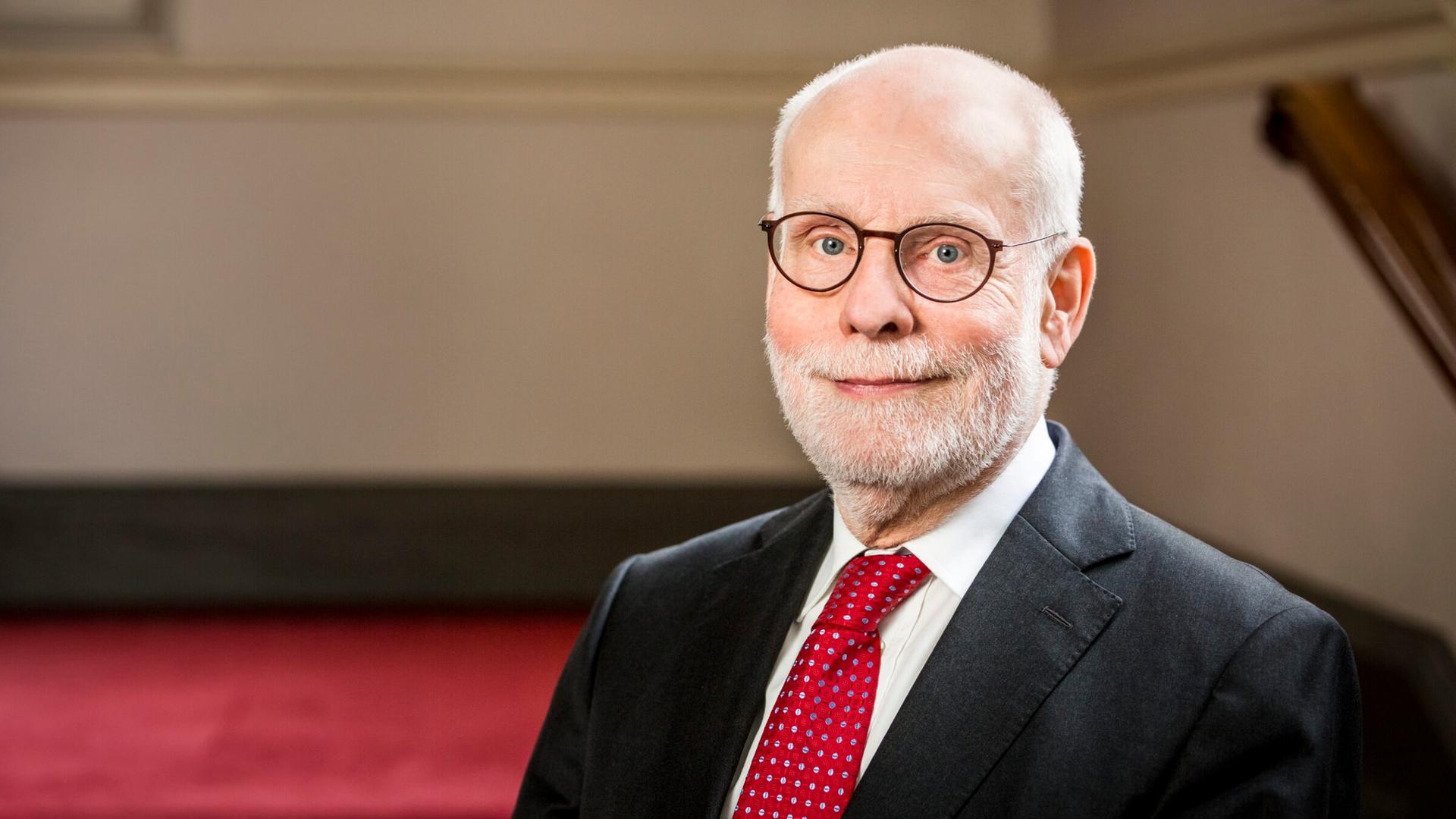 Ton Kopmann sitzt mit Brille in einem Treppenhaus und blickt freundlich in die Kamera.