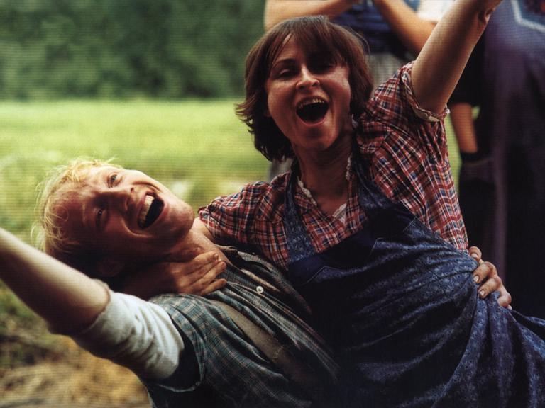 Sophie Rois lacht ausgelassen zusammen mit Simon Schwarz auf einem Feld in einer Szene des Filmes Siebtelbauern.