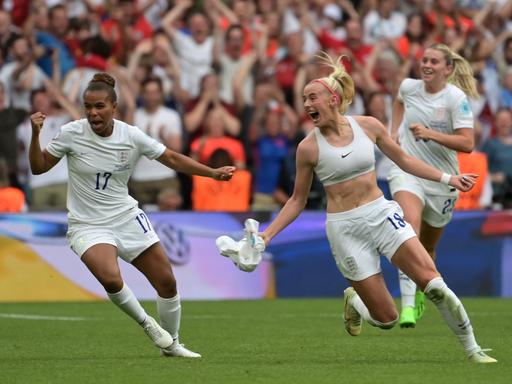 Eine Fußballerin, Chloe Kelly, jubelt auf dem Rasen. Die junge Frau sprintet und hat sich das weiße Trikot ausgezogen. Hose und Stutzen sind auch weiß.