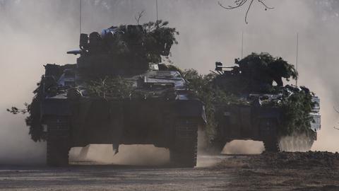 Zwei mit Zweigen getarnte Schützenpanzer vom Typ Marder fahren auf die Kamera zu.