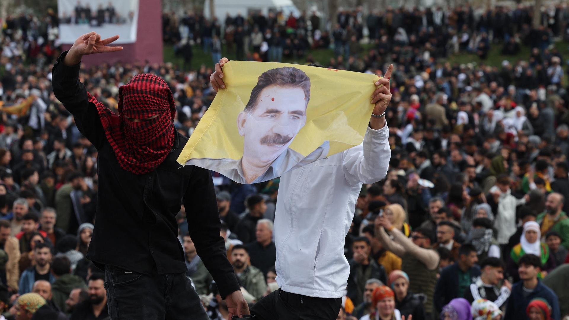 Zu sehen sind Kurden in der Türkei, zwei Männer, einer davon verhüllt, halten ein Porträt von Öcalan hoch Zu sehen sind Kurden in der Türkei, zwei Männer, einer davon verhüllt, halten ein Porträt von Öcalan hoch