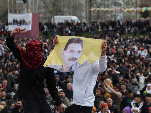 Zu sehen sind Kurden in der Türkei, zwei Männer, einer davon verhüllt, halten ein Porträt von Öcalan hoch