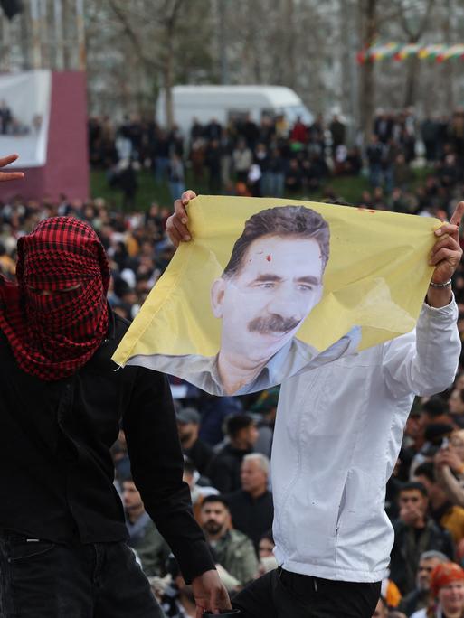 Zu sehen sind Kurden in der Türkei, zwei Männer, einer davon verhüllt, halten ein Porträt von Öcalan hoch