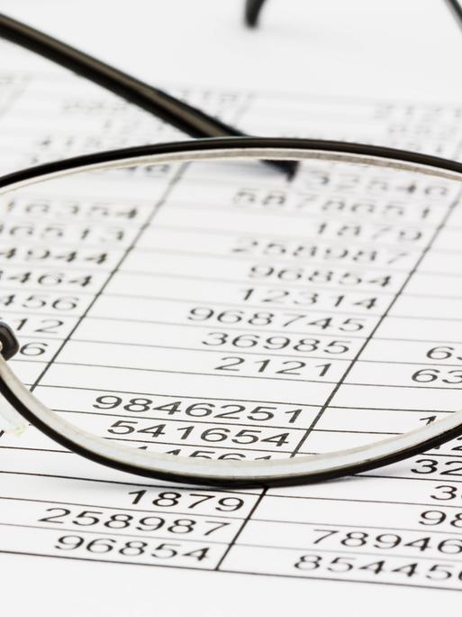 Durch ein Brillenglas ist eine Tabelle mit Zahlenkolonnen zu sehen.