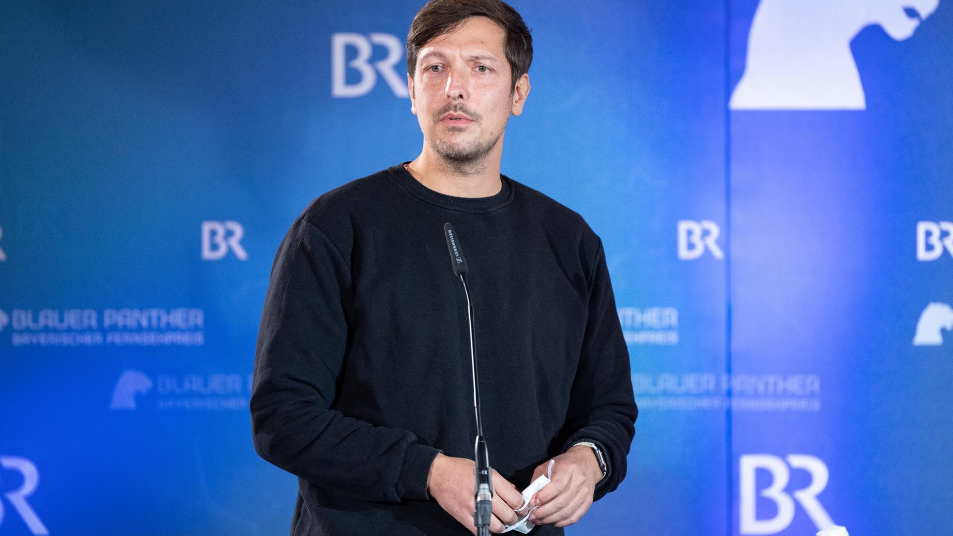 Der Journalist Thilo Mischke steht bei der Verleihung des Bayerischen Fernsehpreises auf der Bühne vor einer blauen Wand, die mit "BR" beschriftet ist.