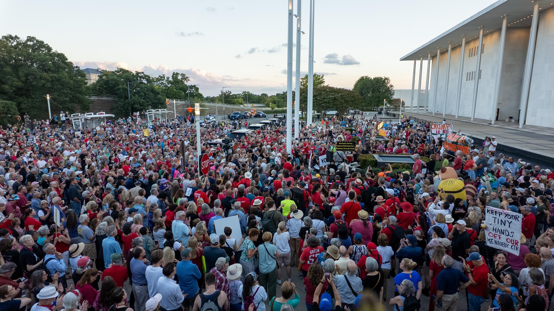 Demonstranten stehen bei Abendlicht vor dem hellen Bau des Kennedy Center.