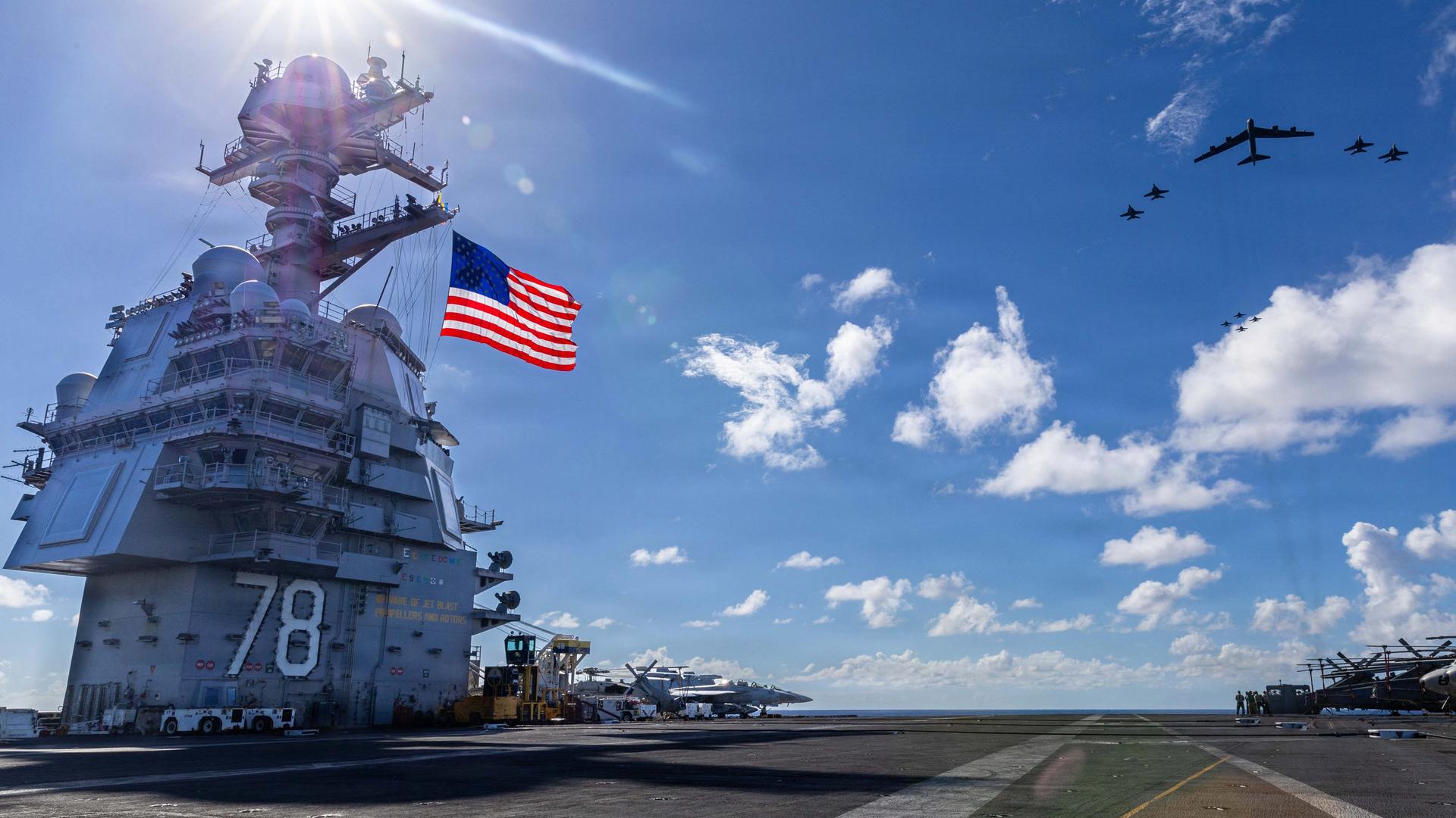 Der größten Flugzeugträger der Welt mit einer US-Flagge vor blauem Himmel und Militärflugzeugen