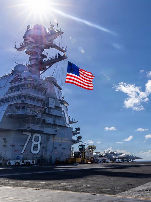 Der größten Flugzeugträger der Welt mit einer US-Flagge vor blauem Himmel und Militärflugzeugen