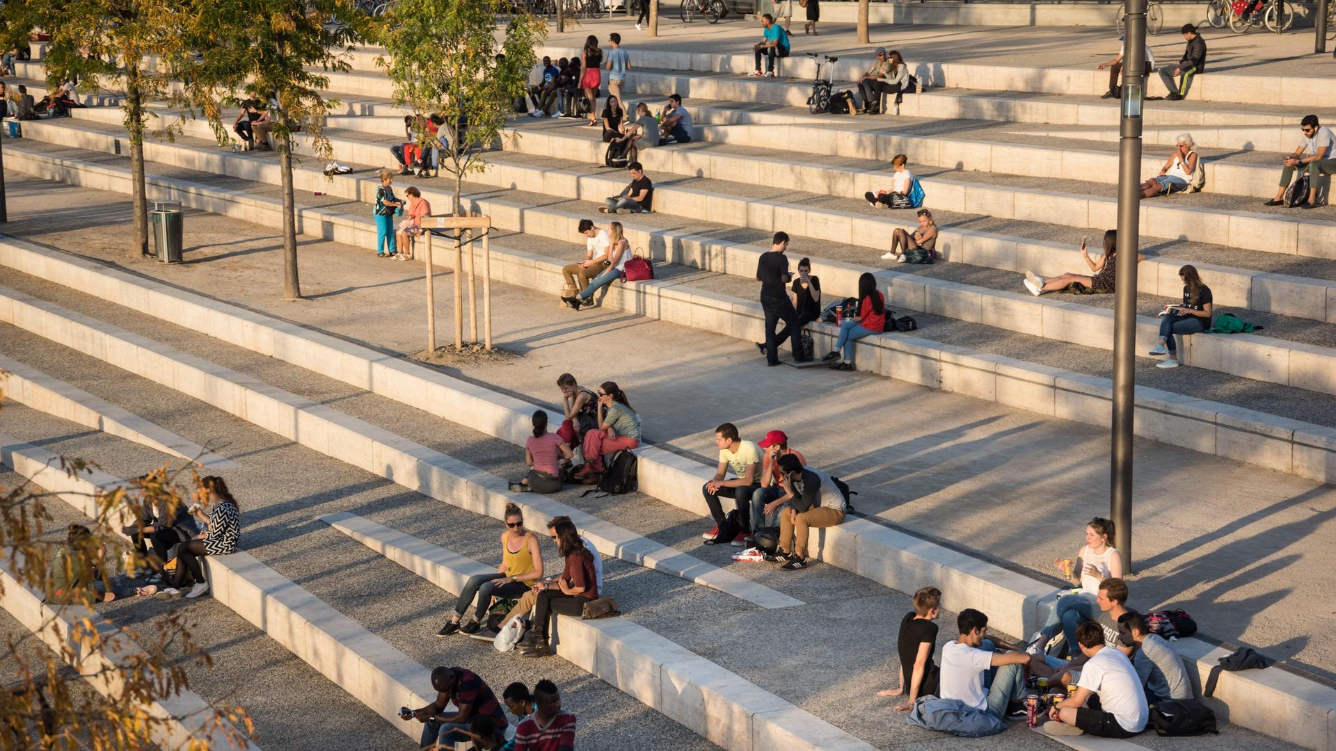 Gruppen von Jugendlichen sitzen auf einer großen Streintreppe mit breiten Stufen und unterhalten sich.