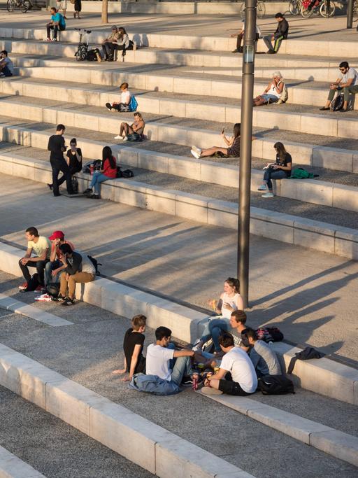 Gruppen von Jugendlichen sitzen auf einer großen Streintreppe mit breiten Stufen und unterhalten sich.
