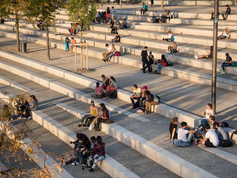 Gruppen von Jugendlichen sitzen auf einer großen Streintreppe mit breiten Stufen und unterhalten sich.