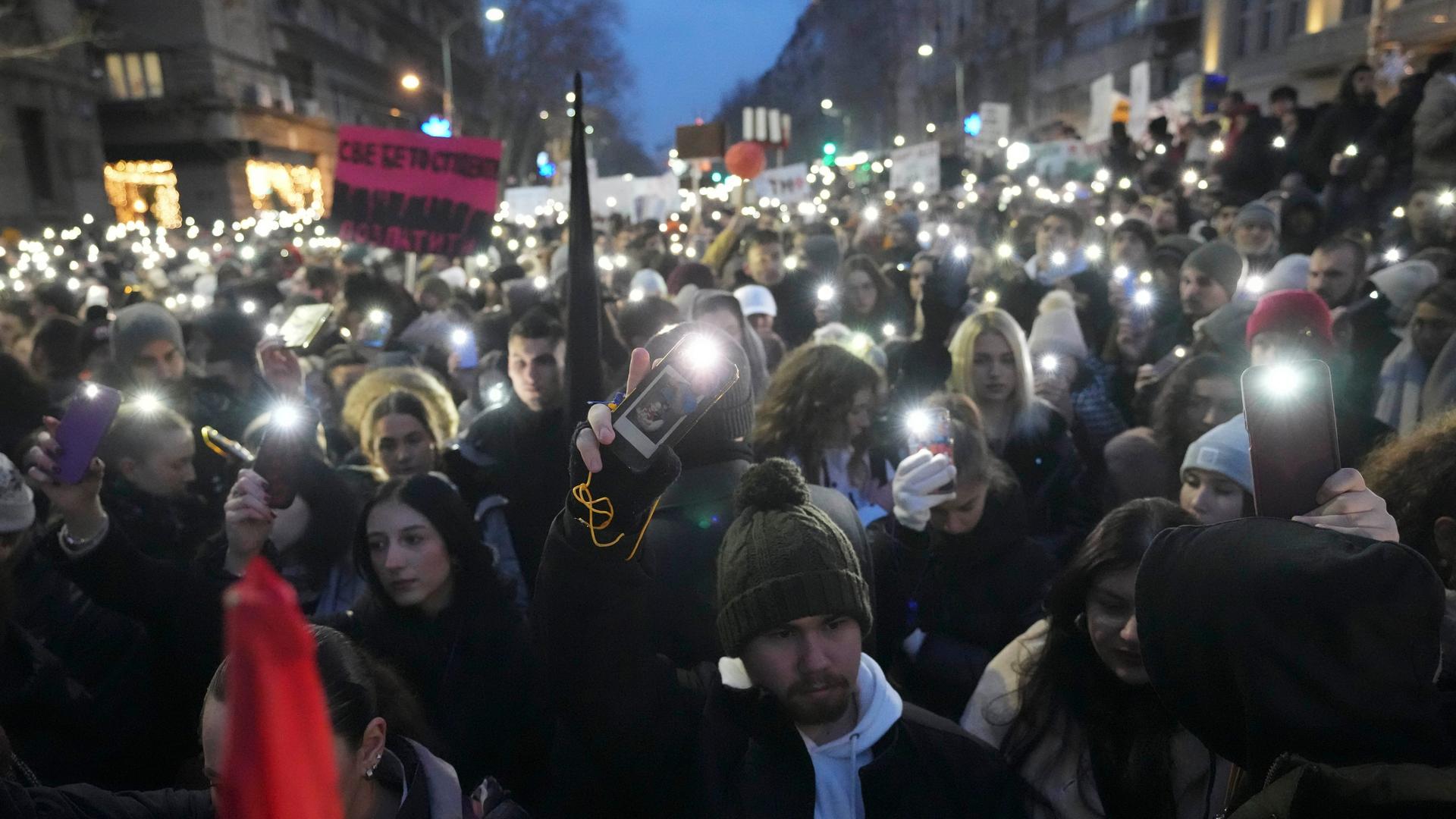 Menschen versammeln sich vor dem Gebäude des serbischen Verfassungsgerichts während einer Demonstration zu dem Bahnhofsdacheinsturz von Novi Sad. Es ist dunkel, man sieht Handylichter leuchten.