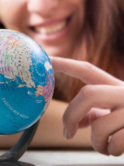 ILLUSTRATION - Eine junge Frau sitzt am 07.03.2019 in Berlin an einem Tisch und schaut auf einen kleinen Globus (gestellte Szene). Foto: Franziska Gabbert