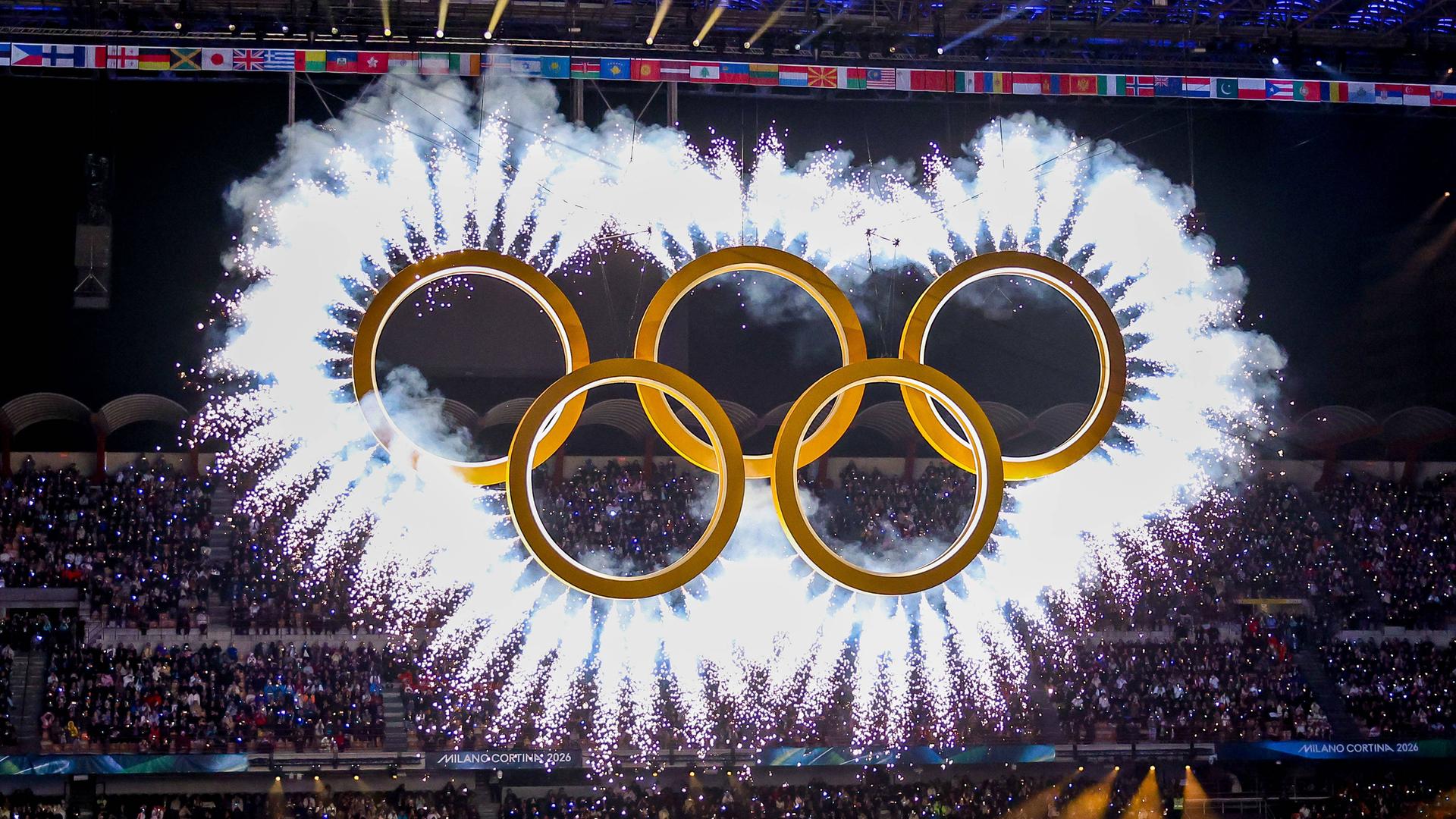 Während der Eröffnung der Olympischen Winterspiele im Mailänder Stadion sind die goldfarbenen Olympischen Ringe umgeben von einer weißen Wolke aus Leuchtfeuern.