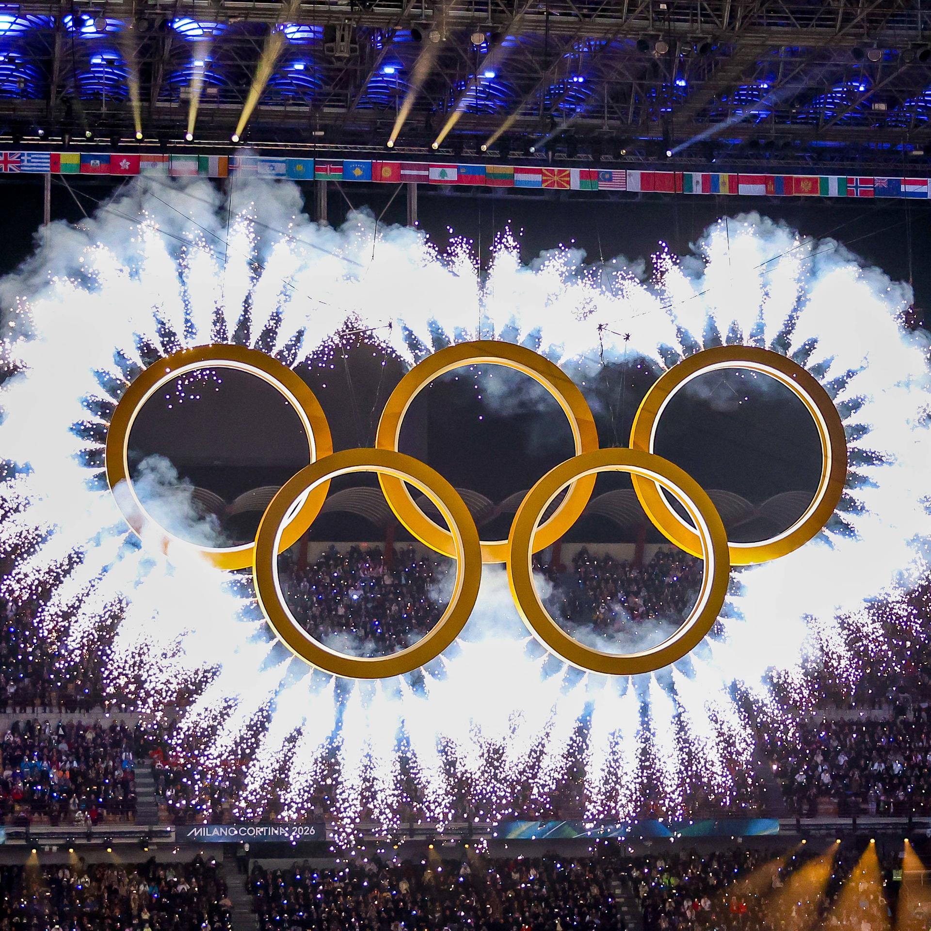 Während der Eröffnung der Olympischen Winterspiele im Mailänder Stadion sind die goldfarbenen Olympischen Ringe umgeben von einer weißen Wolke aus Leuchtfeuern.