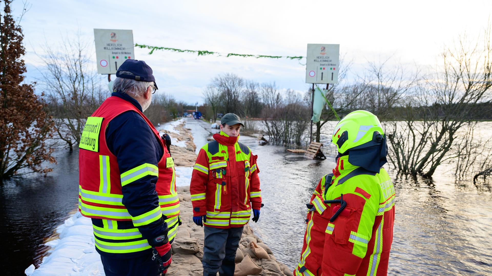 Drei Feuerwehrleute stehen auf einem schmalen Damm im Hochwasser.